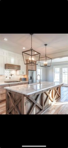 a large kitchen with an island in the middle and two pendant lights hanging from the ceiling