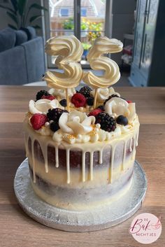 a birthday cake with white frosting and berries on top is sitting on a table