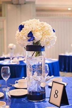 a vase with white and blue flowers is on a table set for an elegant dinner