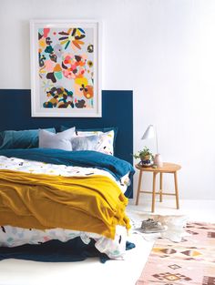 a bed with blue and yellow sheets in a white room next to a small table