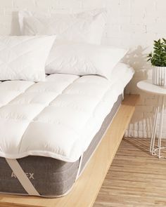 a bed with white pillows on top of it next to a side table and chair