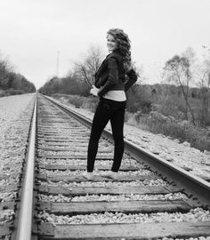 a woman standing on train tracks in black and white