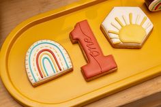 a yellow tray with cookies and cupcakes that say 1 in the shape of a rainbow