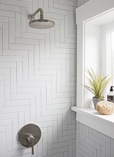 a white tiled bathroom with a shower head, window and potted plant in the corner