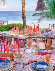 a table set up for an outdoor dinner on the beach with pink and orange napkins