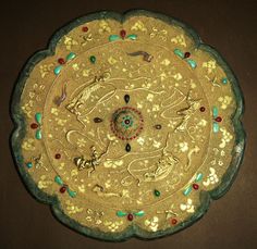 a decorative plate with gold and green designs on it's sides, sitting on a brown surface