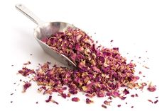 a spoon filled with crushed pink flowers on top of a white table