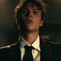 a young man with curly hair wearing a suit and tie in a dimly lit room