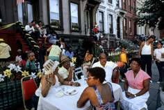 many people are sitting at tables outside on the sidewalk and in front of some buildings