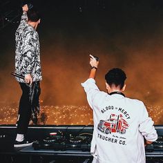 two men standing on stage with their arms in the air and one man holding up his cell phone