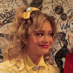 a woman with blonde hair wearing a yellow shirt and a bow in her hair is smiling