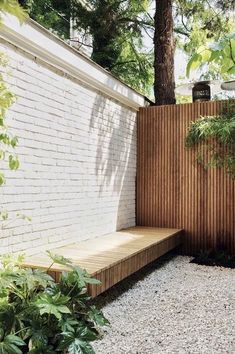 a wooden bench sitting next to a white brick wall and green trees in the background