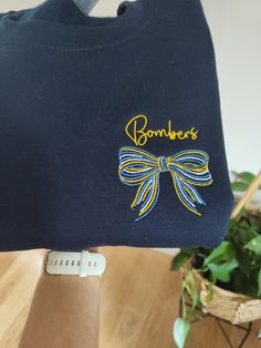 Customize this shirt with your school colors and team name!  A cute multicolored bow is made in 3 colors of your choice.  Above the bow, the name of the school team (ex. Bears, Mustangs, Blue Devils...) is embroidered in a script font (another font available in a different listing in my shop!)  A great gift for a daughter, teacher, bestie, little sister (is there a bigger fan than a little sister watching her siblings play? just about anyone! Perfectly customized it the school colors of your fav School Spirit T-shirt With Embroidered Graphics, Customizable Blue School Spirit Tops, Casual School T-shirt With Embroidered Graphics, Customizable Casual T-shirt For Cheerleading, School T-shirt With Embroidered Text And Crew Neck, School Spirit Tops With Letter Embroidery, Blue T-shirt With Embroidered Graphics For School Spirit, Casual School Tops With Letter Embroidery, Casual Tops With Letter Embroidery For School