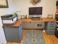 a computer desk with drawers and a printer on it in front of a wall mounted monitor