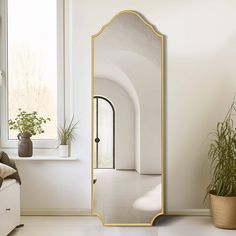 a large mirror sitting next to a window on top of a white floor near a potted plant