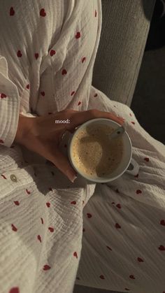 a woman is holding a cup of coffee in her hand while sitting on the couch