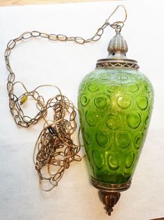 a green vase sitting on top of a wooden table next to a metal chain necklace