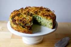 a quiche with cheese and spinach is on a white cake plate next to a knife