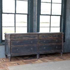 an old dresser is sitting in front of two large windows and a rug on the floor