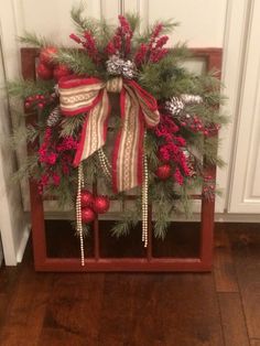 a christmas wreath with red balls and pine cones on a wooden crate in front of a door