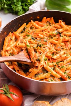 a pan filled with pasta and vegetables on top of a table next to bread slices