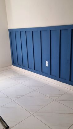 an empty room with white tile and blue paneling on the wall, next to a broom