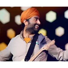 a man wearing an orange turban and holding a guitar in his right hand