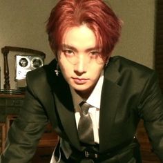 a man with red hair wearing a suit and tie in a living room next to a radio