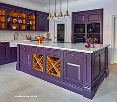 a kitchen with purple cabinets and marble counter tops, wine rack on the island in the center