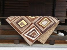 two quilts sitting on top of a wooden bench next to each other in front of a log cabin