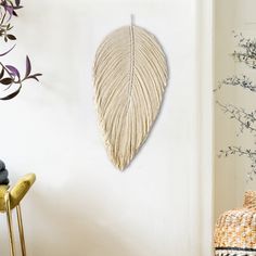 a white wall with a large leaf hanging on it's side next to a yellow chair