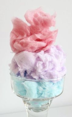 cotton candy in a glass bowl on top of a white tablecloth with pink, blue and purple colors