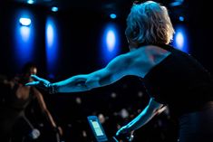 a woman on a stationary bike in front of an audience with her arm extended out