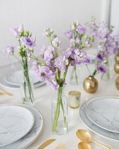 the table is set with purple flowers in vases and silverware, along with gold plates