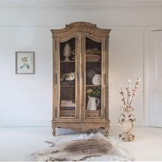 an antique china cabinet with glass doors and shelves in the corner, next to a vase filled with flowers