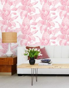 a white couch sitting next to a table with a plant on top of it in front of a pink wallpaper