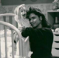 a man holding a baby up to his face while standing next to a crib