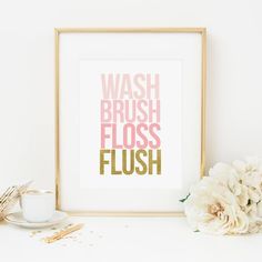 a white vase with flowers sitting next to a framed print that says wash brush floss flush