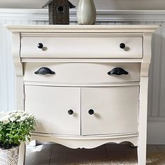 a white dresser sitting in a living room next to a potted plant and birdhouse