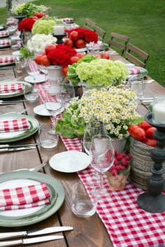 a long table is set with red and white checkered placemats, plates, silverware, and flowers