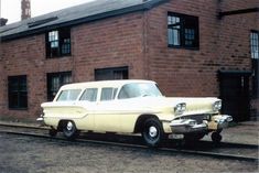 an old car is parked in front of a brick building on the side of the road