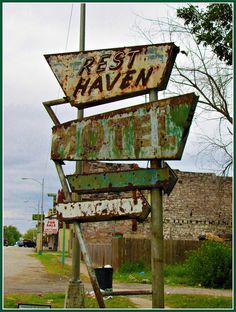 an old rusted sign sitting on the side of a road next to a building