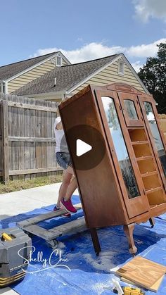 a man is working on a wooden cabinet in front of a house with blue tarp