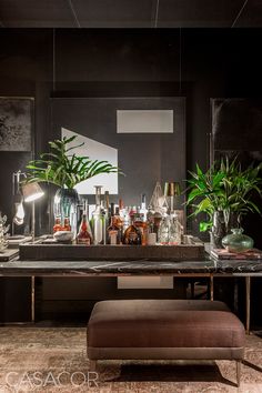 a bar with plants and liquor bottles on the counter in front of it, along with a foot stool