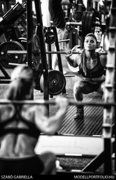 a woman squats on the ground while holding a barbell in her hand and looking at