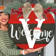 a woman holding up a welcome sign in front of a door with christmas decorations on it