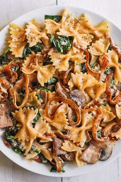 a white plate topped with pasta and spinach covered in mushrooms, cheese and seasoning