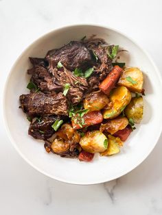 a bowl filled with meat and vegetables on top of a white countertop next to a fork