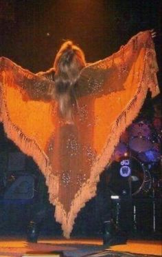 a woman in an orange dress on stage with her arms spread out to the side