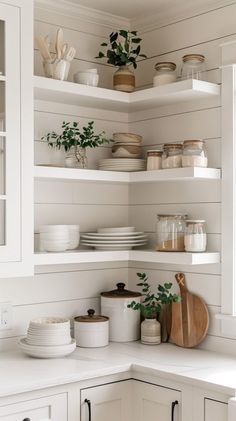 the shelves in this kitchen are filled with white dishes and pots, while plants sit on top of them